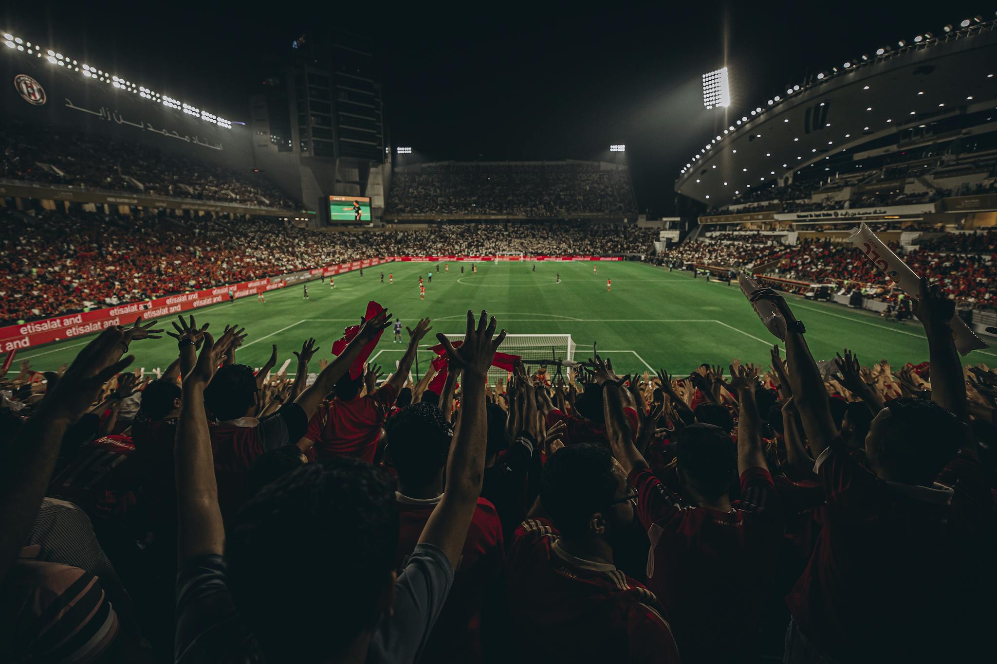 Lively football match with cheering fans in Abu Dhabi stadium at night.